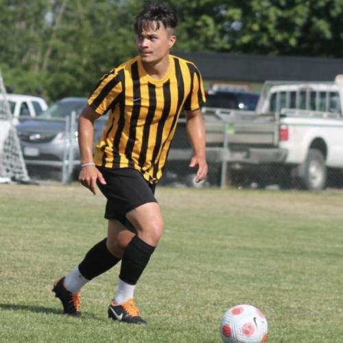 A young man in yellow-and-black striped shirt playing soccer. 