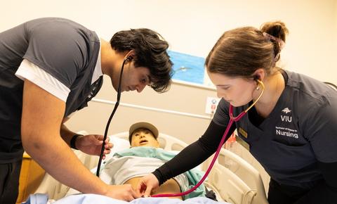 2 students checking manikin abdomen with stethoscopes